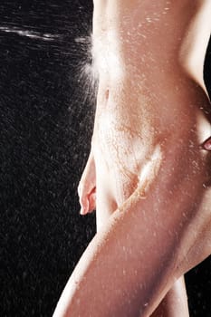 Water splashing on fit nude female body over black