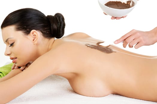 Pretty young woman relaxing being massaged in spa saloon with chocolate. Isoalted on white