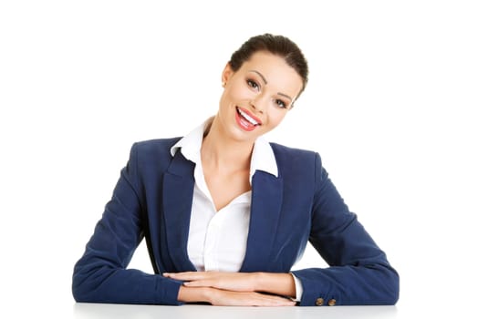 Pretty happy young business woman is sitting at the desk, isolated on white