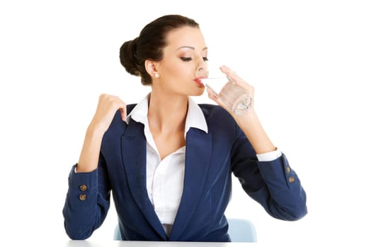 Pretty business woman sitting at the desk and drinking mineral water from glass