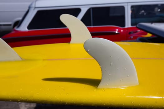 Yellow surfboard keel fins detail eith red retro car in background in California
