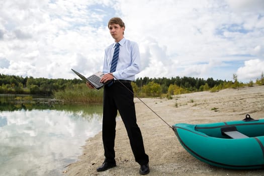 Dressed man drags boat over sandy lake shore