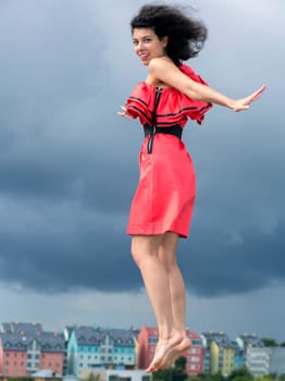 Woman in nice dress jumping on city background