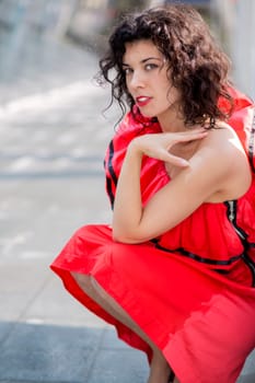 Woman in red dress squatting at sunny square