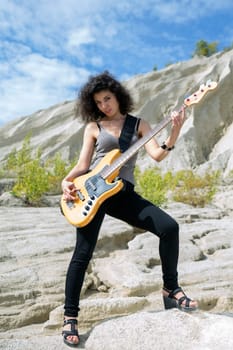 Woman play yellow bass guitar on sandy background