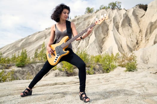 Woman on sandy background with yellow bass guitar
