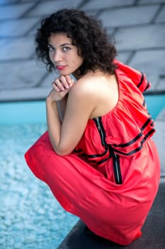 Woman in nice dress squatting near swimming pool