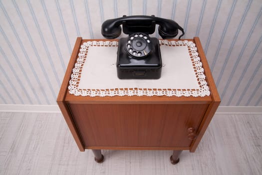 Black rotary dial telephone on a piece of furniture with old fashioned striped wallpaper