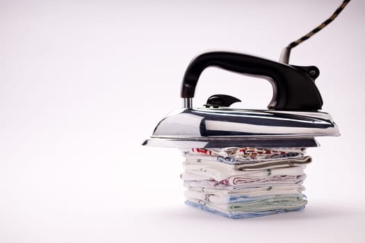 old fashioned electric iron with a black plastic handle and steel base lain on a pile of handkerchiefs in a natural light background