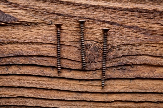 A set of three bronzed copper screws on a dark coarse-grained wooden background