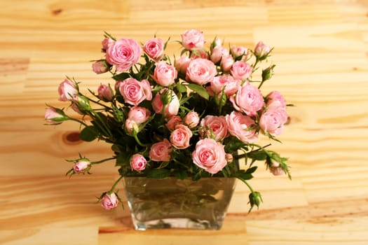 Bunch of small pink Roses in a glass vase over a wooden table..