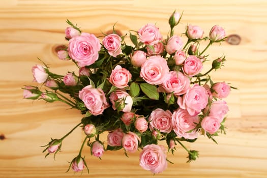 Bunch of small pink Roses in a glass vase over a wooden table..