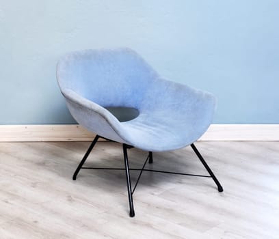 Upholstered vintage blue velvet armchair with curved modular design and metal legs in a room with parquet floor and matching wall color