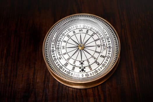 Old round brass magnetic vintage compass with glass dial lying on a wooden board in a high angle view
