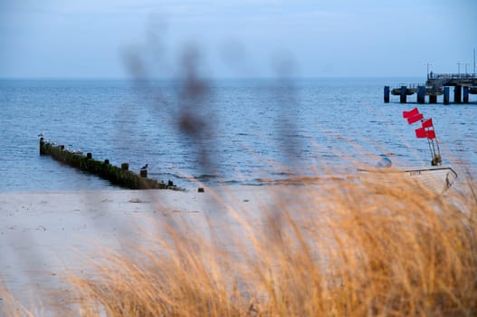 View over the dunes to the white sandy beach on the island of Usedom with dune grass in the blurred foreground and a small fishing boat at a groyne  Background