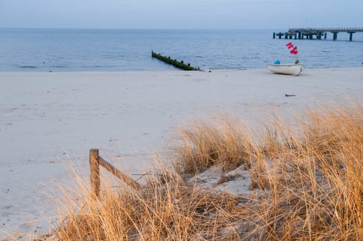 View over the Dühnen to the white sandy beach on the island of Usedom with dunning grass in the blurred foreground and a small fishing boat at a groyne  Background