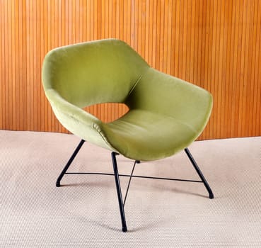 Upholstered green velvet curved vintage armchair with plush fabric and metal legs in a panelled living room