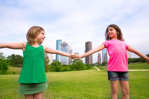Two sister girls friends playing holding hand in urban modern skyline on park lawn