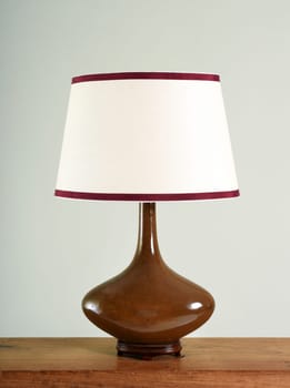 Elegant brown bulbous vintage lamp with white shade with matching colored trim on a wooden table