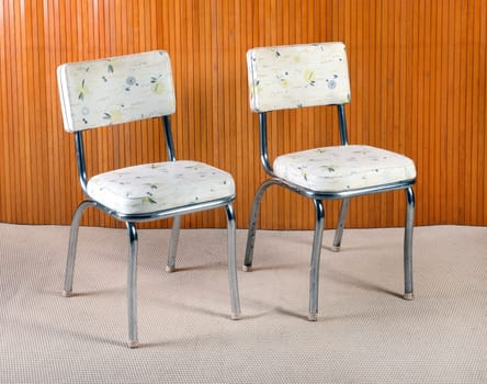 Still Life of Retro Chairs with Metal Bases and Patterned Seat Upholstery in Room with Beige Carpet and Wood Wall Paneling