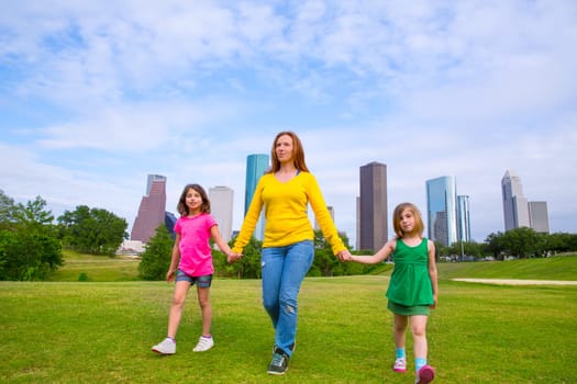 Mother and daughters walking holding hands on modern city skyline over park green lawn