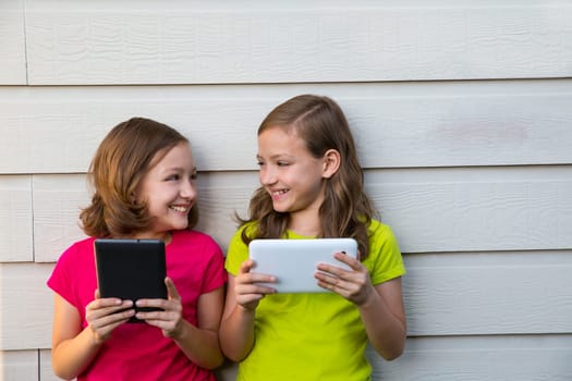 Twin sister girls playing with tablet pc happy on white wall looking each other