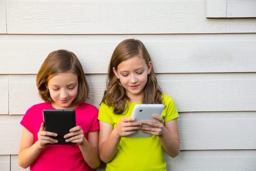 Twin sister girls playing with tablet pc happy on white wall looking screen