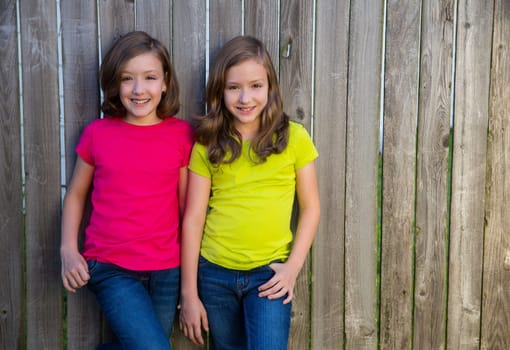 Twin sister girls with different hairstyle posing on wood backyard fence