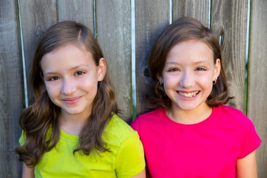Happy twin sisters with different hairstyle smiling on wood backyard fence