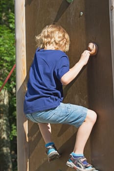 The blond boy climbs the climbing wall in summer day.