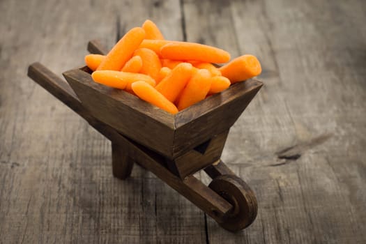 Fresh carrots in a miniature wheelbarrow on wooden background.