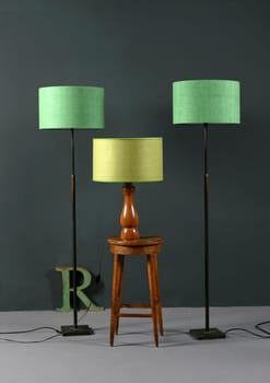 Three vintage lamps with green shades, two matching floor lamps flanking a wooden table lamp on a stool in a grey room in an interior decor concept
