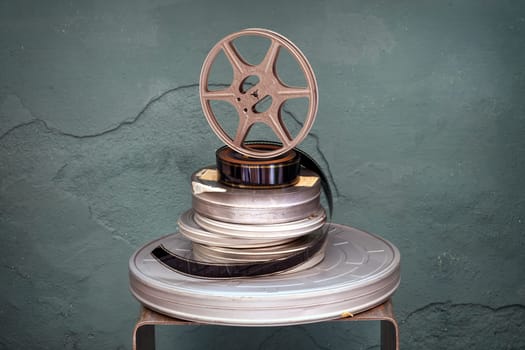 Old stacked vintage movie films of assorted diameters with a projector reel standing upright on top over a textured green background with vignette in an entertainment concept