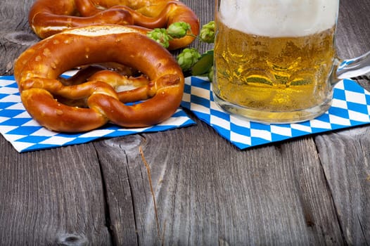 A glass of beer,pretzels and some hop cones on an old rustic wooden table