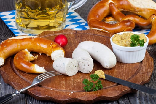 Round wooden board with white sausage,pretzel,mustard and radishes and a glass of beer on an old rustic wooden table