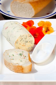 Homemade nasturtium herb butter on a plate with a piece of baguette and sea salt on a rustic wooden table