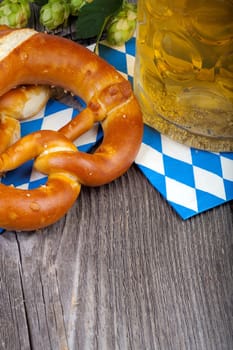 A glass of beer,pretzels and some hop cones on an old rustic wooden table