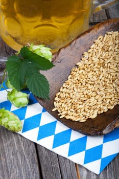 Glass of beer,hops and grain on a wooden shovel on an old rustic wooden table