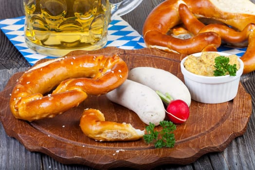 Round wooden board with white sausage,pretzel,mustard and radishes and a glass of beer on an old rustic wooden table