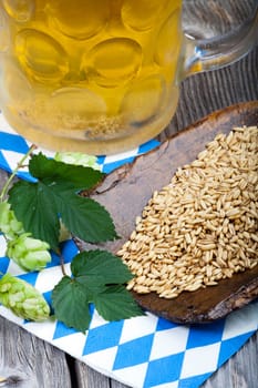 Cool beer in a glass,hop cones and grain on a wooden shovel on an old rustic wooden table