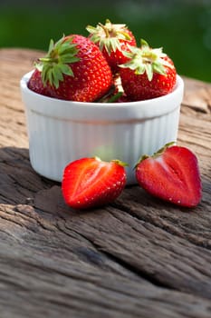 Delicious fresh strawberries in a white porcelain bowl on a rustic wooden table with text space in the lower part of the picture