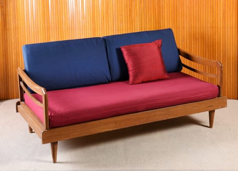 Upholstered red and blue vintage sofa with a wooden frame and armrests in a wood panelled room