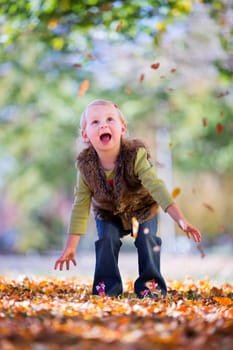 cute little girl throwing autumn leaves