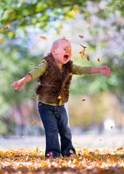 cute little girl playing with autumn leaves