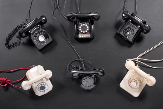 Collection of old vintage rotary dial up telephone instruments in white and black viewed from overhead on a dark grey background