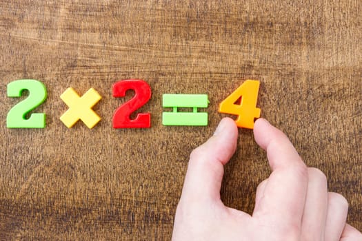 Solving simple mathematical formula. Hand with colored numbers on the wooden table