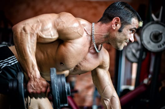 Muscular male bodybuilder working out in gym, exercising triceps leaning on a bench
