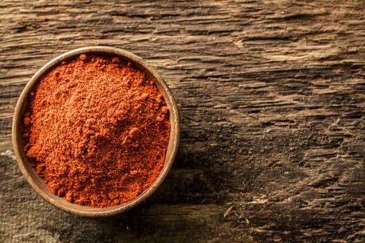 Overhead close up view of a bowl of ground red cayenne pepper on a weathered heavily textured wooden background with copyspace