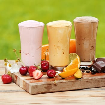 Three glasses of tasty various natural protein cocktails surrounded by fresh fruits