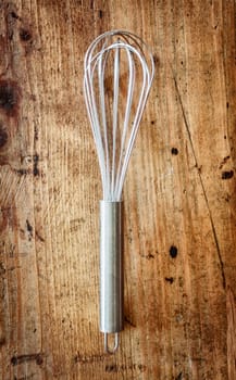 Metal whisk or eggbeater for whipping and whisking cooking ingredients lying on a textured wooden background with woodgrain